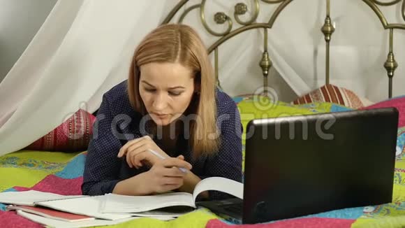 美女在家在线教育学生在床上有工作簿和笔记本电脑慢动作视频的预览图