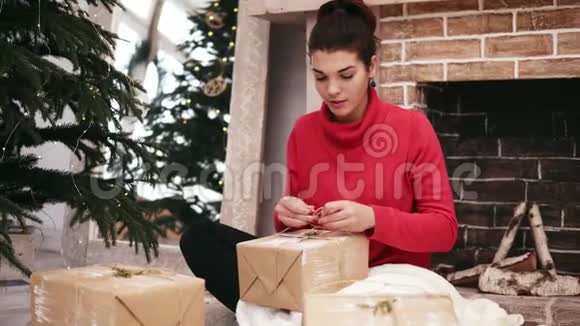 美丽的微笑女人把圣诞礼物包在家中的圣诞树和壁炉旁然后把礼物放在视频的预览图