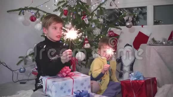 两个孩子点燃了火花在圣诞树的背景下树灯和花环视频的预览图