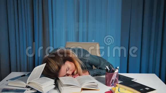 一个穿牛仔衬衫的女学生累了在一张有书的桌子上睡着了视频的预览图