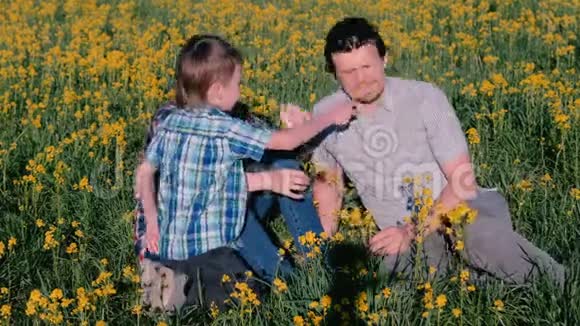 妈妈爸爸和儿子一起玩黄花坐在草地上家庭散步视频的预览图