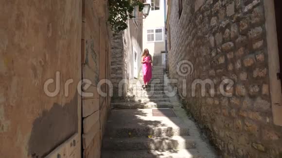穿着粉色衣服的女人走在狭窄的老石街的楼梯上视频的预览图