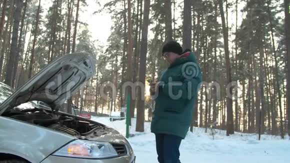 冬天一个人修理一辆破汽车一名男子站在打开的汽车引擎盖旁正在寻找破损处视频的预览图