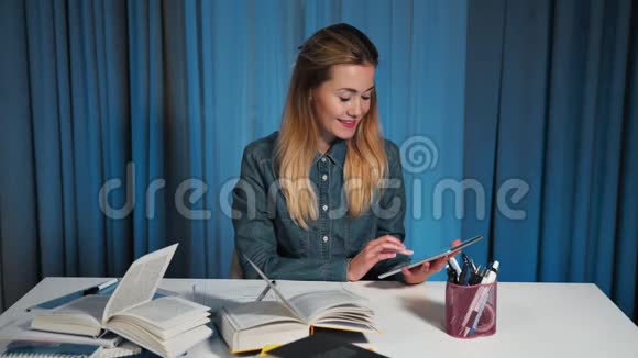 一个穿牛仔衬衫的快乐女学生使用平板电脑并重写工作簿中的信息视频的预览图