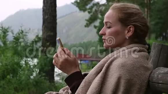 年轻女子在靠近山河的公园长椅上放松用智能手机发送信息视频的预览图