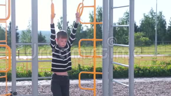 七岁的男孩挂在操场上的体操戒指上视频的预览图