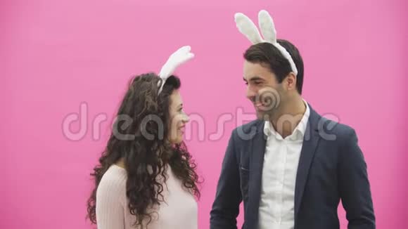 站在粉红色背景上的年轻夫妇在这段时间里他们的耳朵都是乌合之众看每一个视频的预览图