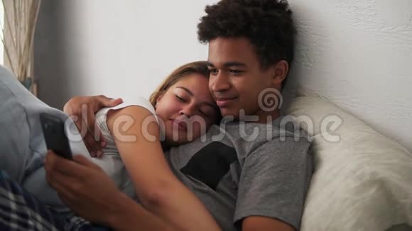 迷人的多民族年轻夫妇在卧室放松智能手机互相拥抱慢镜头视频的预览图