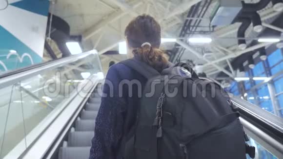 年轻的旅游女孩带着背包带着手提箱沿着自动扶梯上了机场等待着飞机的生活方式视频的预览图