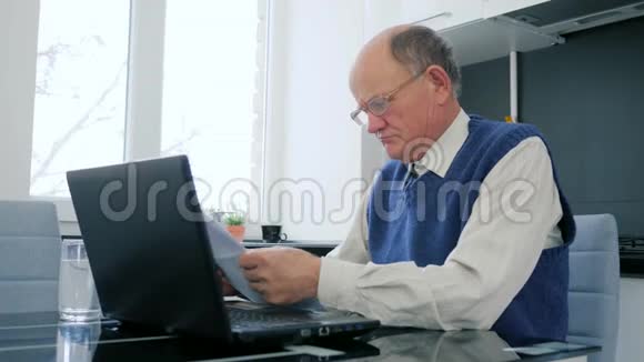 远程商务老人在互联网上的笔记本电脑上工作家里的办公室里有文件视频的预览图
