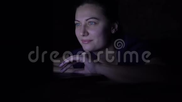 一个女孩在晚上躺在家里的床上用移动电脑在线购买孤立光视频的预览图