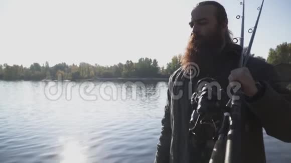 长胡子的渔夫拿着钓竿在河岸上散步慢动作视频的预览图