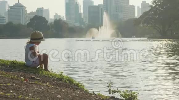穿着乡村风格帽子的小女孩在公园湖里慢动作喂鱼视频的预览图