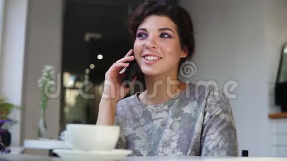 智能手机女人坐在咖啡馆里桌上放着一杯咖啡一边打电话她笑着笑着视频的预览图