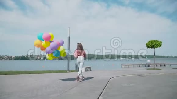 快乐的年轻女孩带着五颜六色的气球在湖岸散步4K视频的预览图