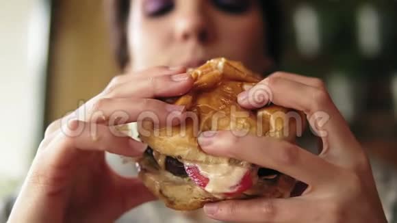 近距离观看年轻女子咬大美味多汁汉堡在咖啡馆慢镜头视频的预览图