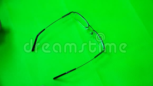 手指折叠眼镜把镜片放在绿色的布上视频的预览图