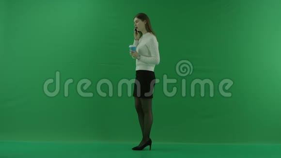 女孩站在她的左边打电话从绿色屏幕上的杯子里喝东西视频的预览图