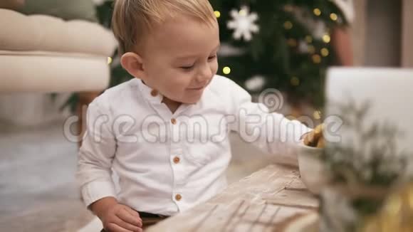 快乐可爱的男孩穿着白色衬衫坐在地板上背景是一棵圣诞树视频的预览图