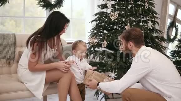 金发可爱的幼儿收到他父亲的圣诞礼物背景上美丽的圣诞树家庭视频的预览图