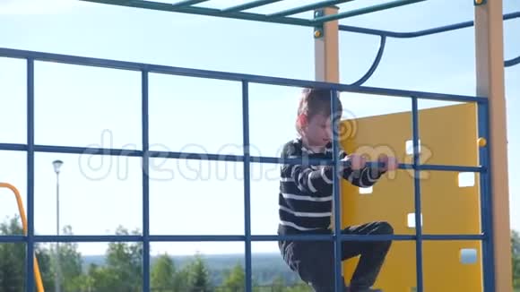 男孩爬在攀岩墙上手里拿着绳子在操场上视频的预览图