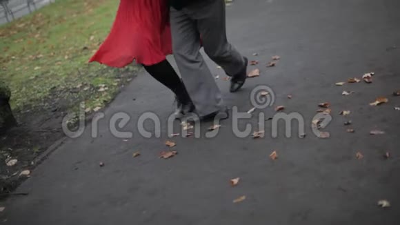 男人女人的腿在铺满黄叶的街道上跳舞视频的预览图