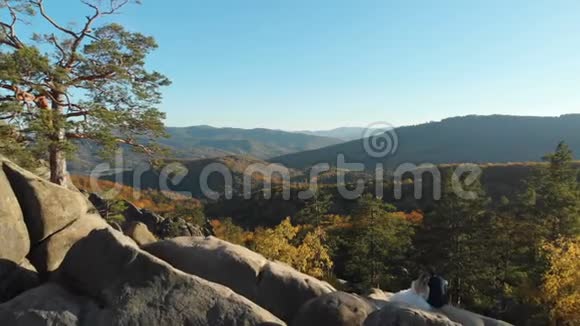爱的一对在日落时分坐在山上的岩石上视频的预览图