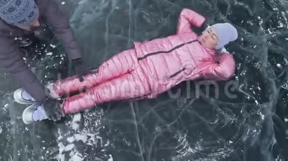 女孩飞起来在冰上翻滚在冰封的湖面上年轻夫妇在冬天散步时玩得很开心视频的预览图