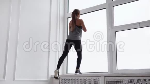 苗条的女人正在大窗户附近做体育锻炼视频的预览图