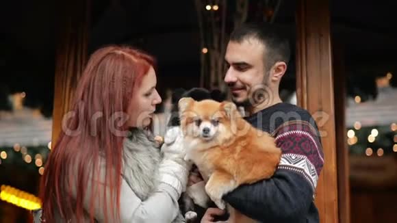 在圣诞节的时候有一对年轻的夫妇在外面玩他们抱着可爱的狗新年快乐理念视频的预览图