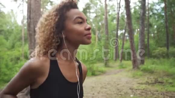 年轻美丽的非洲裔美国妇女卷发在森林里伴着音乐奔跑亲密无间视频的预览图