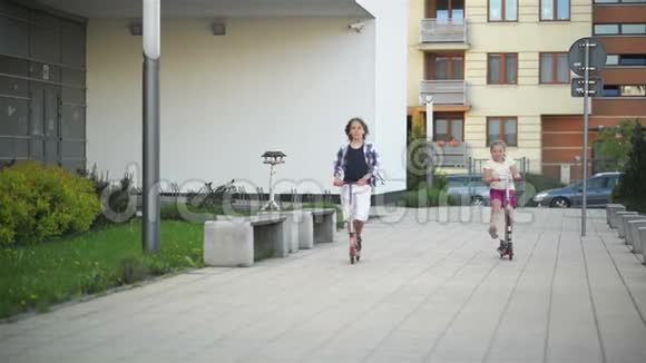 女孩和男孩骑着踢滑板车在户外快乐可爱的孩子们在街上玩耍学习平衡踢板视频的预览图
