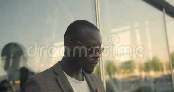 年轻英俊的美国黑人男子的肖像戴着太阳镜在玻璃大厦附近修正了他时髦的夹克视频的预览图