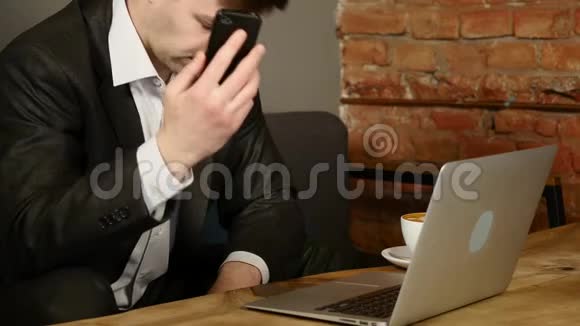 商人在咖啡馆谈论智能手机男人坐在咖啡馆的桌子旁用手机说话笔记本电脑躺在上面视频的预览图
