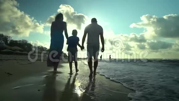 家人在海滩上散步父母和儿子一起沿着海滨散步他们很开心阳光灿烂视频的预览图