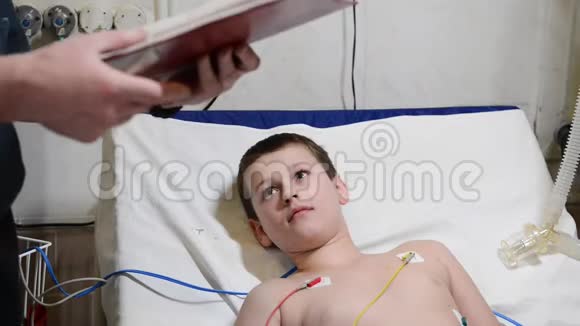 小男孩躺在病床上一边微笑一边听男医生在剪贴板上写字视频的预览图