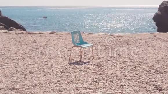 在海滩上靠海的椅子库存古老的孤椅矗立在石滩上映衬着蔚蓝美丽的大海和晴空视频的预览图