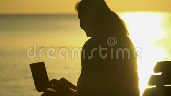 他的女人在电脑上打印那个女人用电脑海洋海岸的剪影视频的预览图
