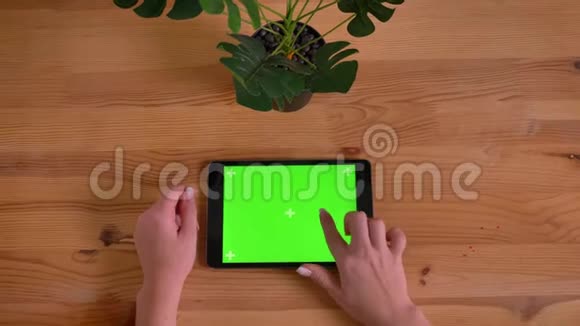 顶部拍摄的女性手打字在绿色屏幕上的水平平板电脑在木桌和植物背景视频的预览图
