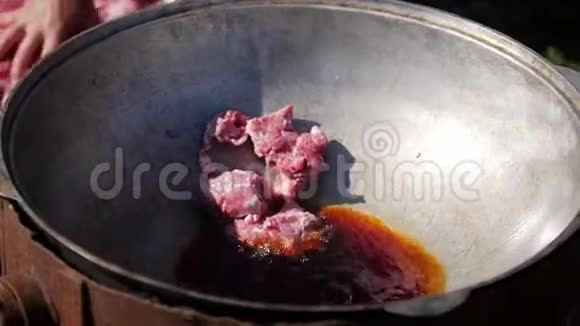 一块块肉扔进燃烧的油锅里在野外徒步旅行时在燃烧的火焰中准备野营食物的过程视频的预览图