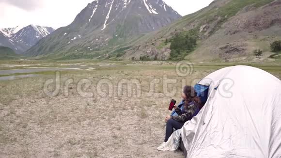 女游客坐在帐篷里一边喝着山背景下的热杯茶视频的预览图
