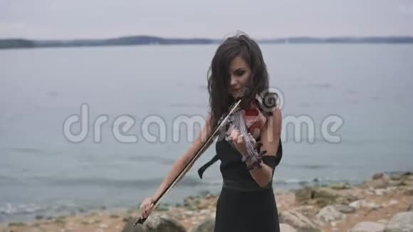 穿黑色连衣裙的漂亮女孩在海上拉小提琴4k的艺术概念视频的预览图