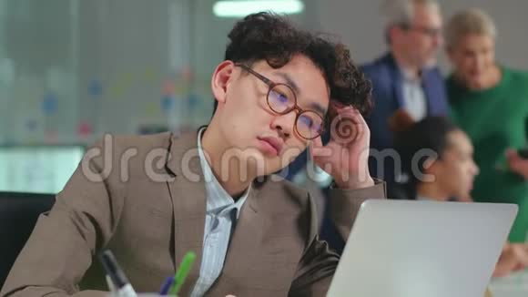 疲惫的亚洲男人在办公室里用笔记本电脑工作视频的预览图