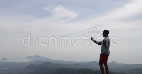 男子登上山顶男子游客在手机后景拍摄晨景视频的预览图