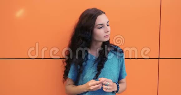 体贴的年轻漂亮女孩长着棕色的长发在橙色的墙壁背景上视频的预览图