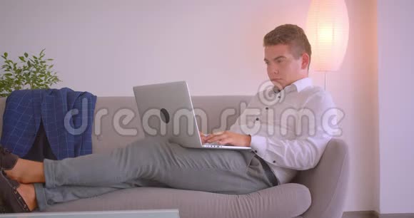 成年白种人商人用笔记本电脑在办公室里悠闲地坐在沙发上的特写照片视频的预览图