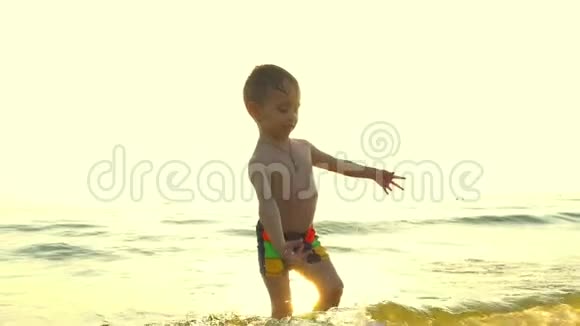 一个孩子在海边在海浪中在日落的背景下慢动作地玩水视频的预览图