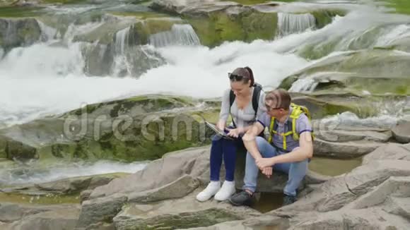 一对年轻的游客在一条山河附近的风景如画的地方欣赏一块石碑技术和旅游概念视频的预览图