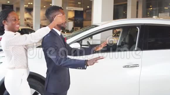 礼物送给心爱的男人女人站在男人后面靠近新汽车惊喜在汽车销售中心视频的预览图