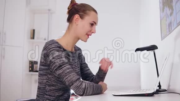 快乐微笑的女人带着笔记本电脑在家里或办公室举行视频会议她挥舞着手视频的预览图